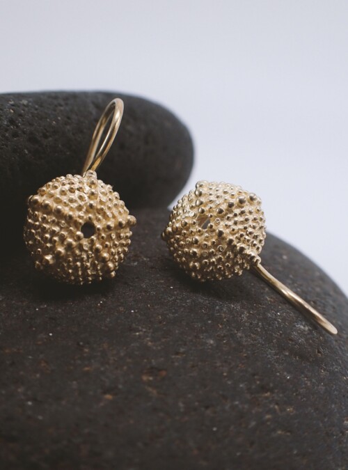 small earrings in a shape of sea urchins placed on a pebble stone