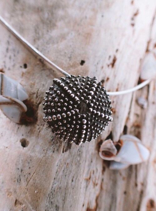 black colored necklace in shape of a sea urchin skeleton placed on driftwood