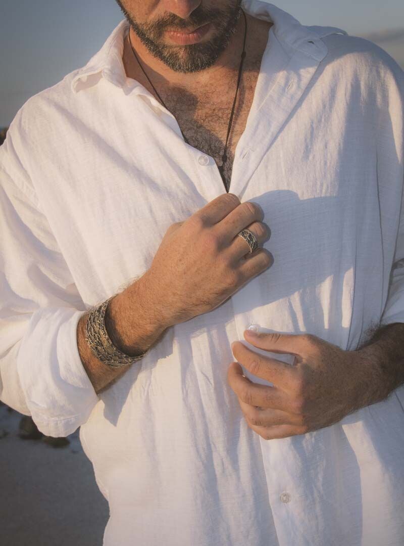 Mann knöpft sein weißes Hemd mit der Hand zu