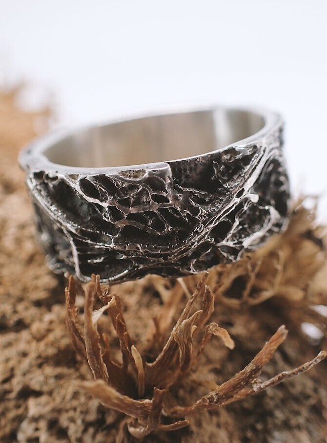 anillo de plata oxidada con textura de raíces colocado sobre una planta seca