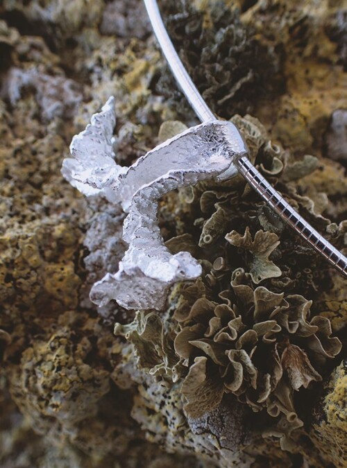 silver pendant on chain placed on a rock covered by lichen
