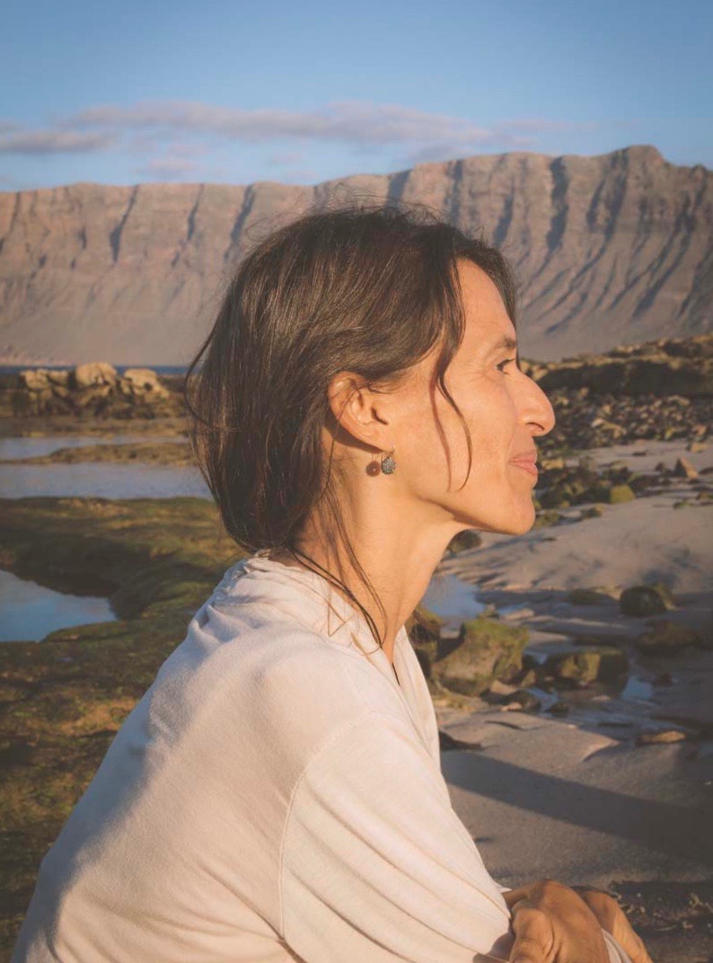 Profil einer Frau, die einen Ohrring aus oxidiertem Silber in Form eines schwarzen Seeigels trägt, mit Famara im Hintergrund