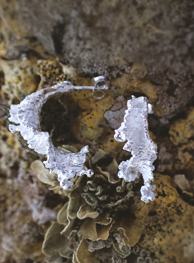 organic shaped silver earrings placed on a volcanic rock