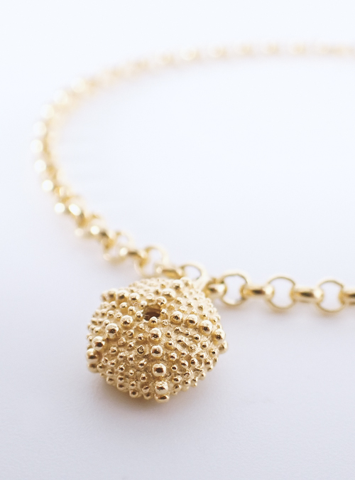 Goldener Anhänger am Armband in Form eines Seeigel-Skeletts