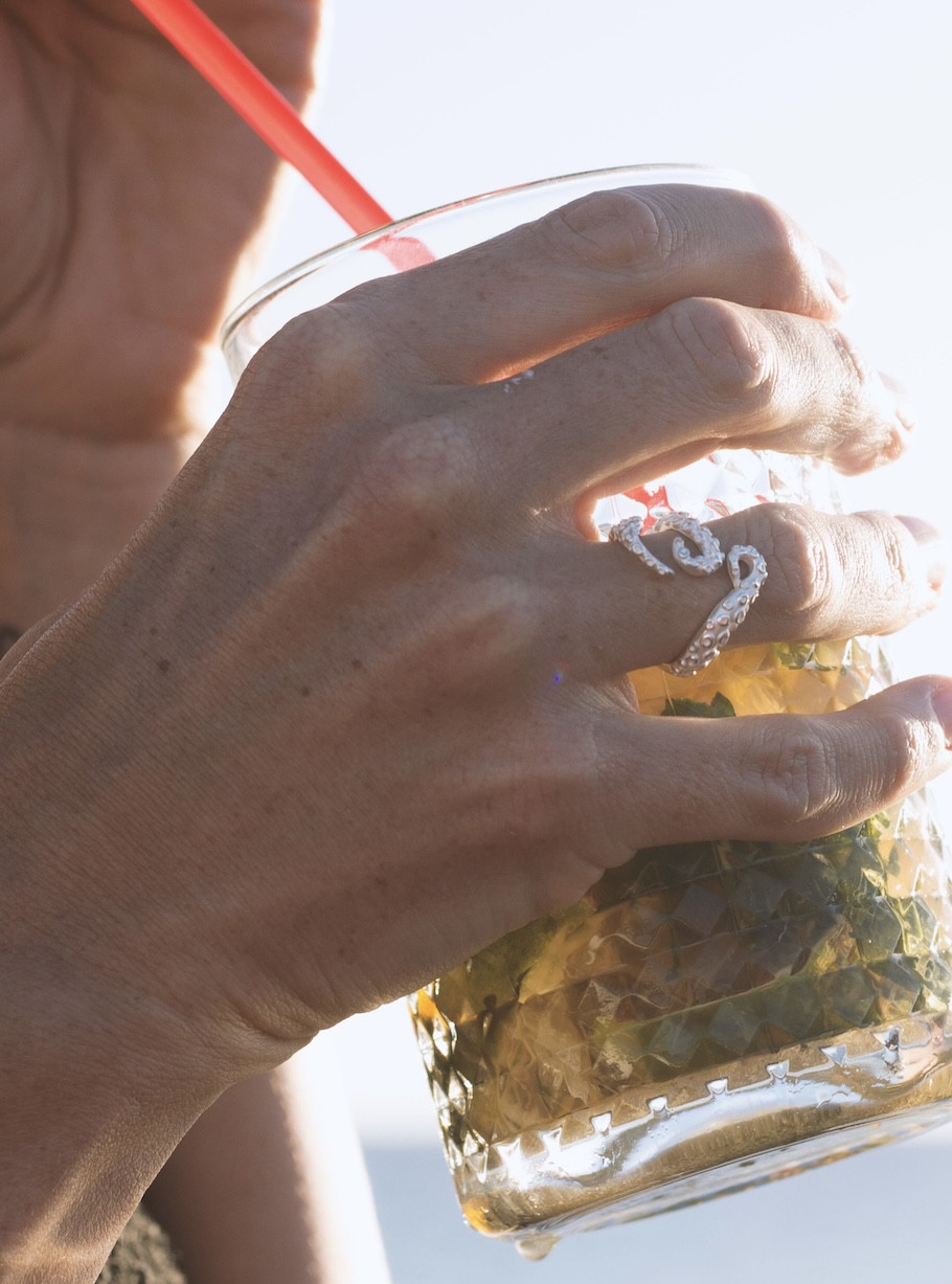 Die Hand der Frau, die den silbernen Krakenring trägt, hält ein Glas